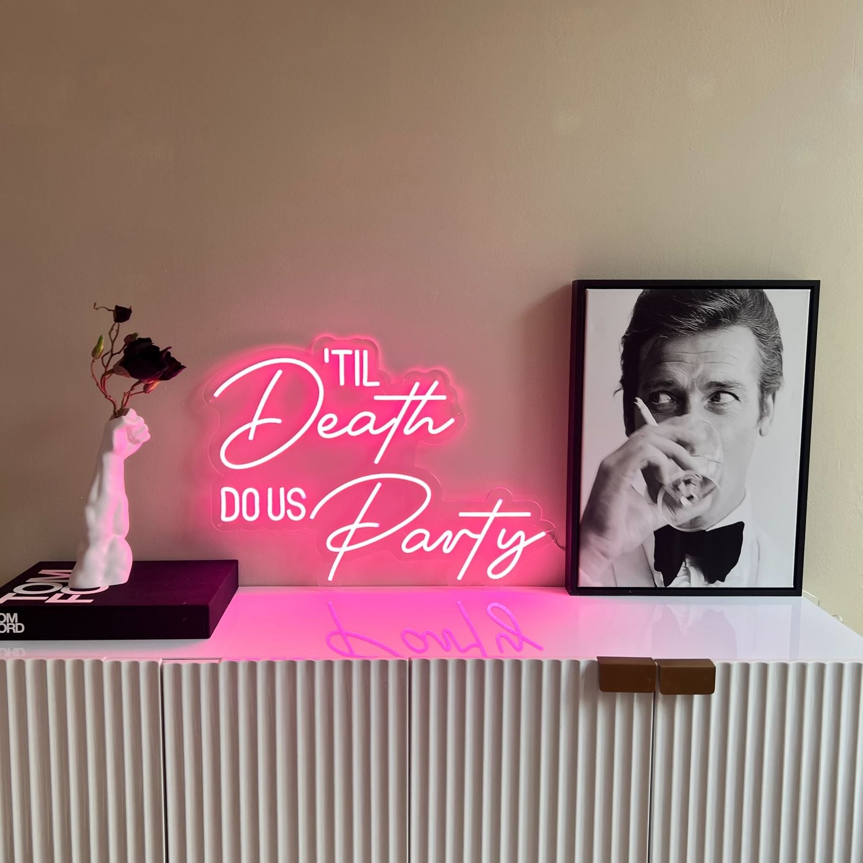 Til Death Do Us Party pink LED neon sign styled with art and flowers in a contemporary interior