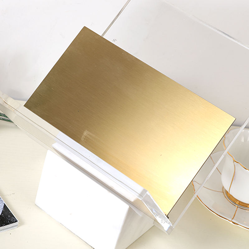 Close-up of the brushed brass shelf and clear acrylic frame on the Folio magazine holder by BAG&BONES.