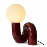 The Burgundy Lune Lamp sculptural table lamp with curved burgundy red resin base and warm white glass globe