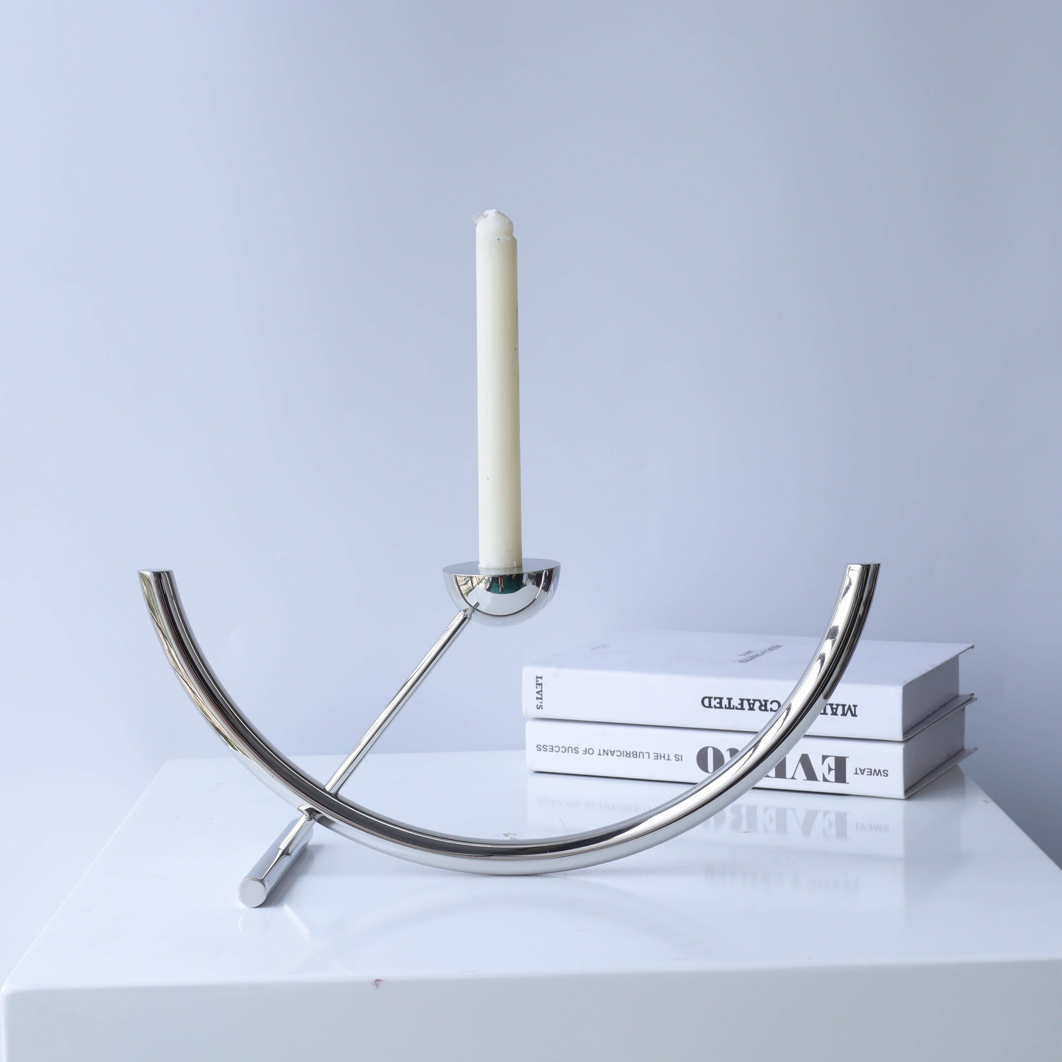 Orbit chrome candle holder by BAG&BONES displayed with a white dinner candle, featuring a polished stainless steel sculptural design in a modern interior.