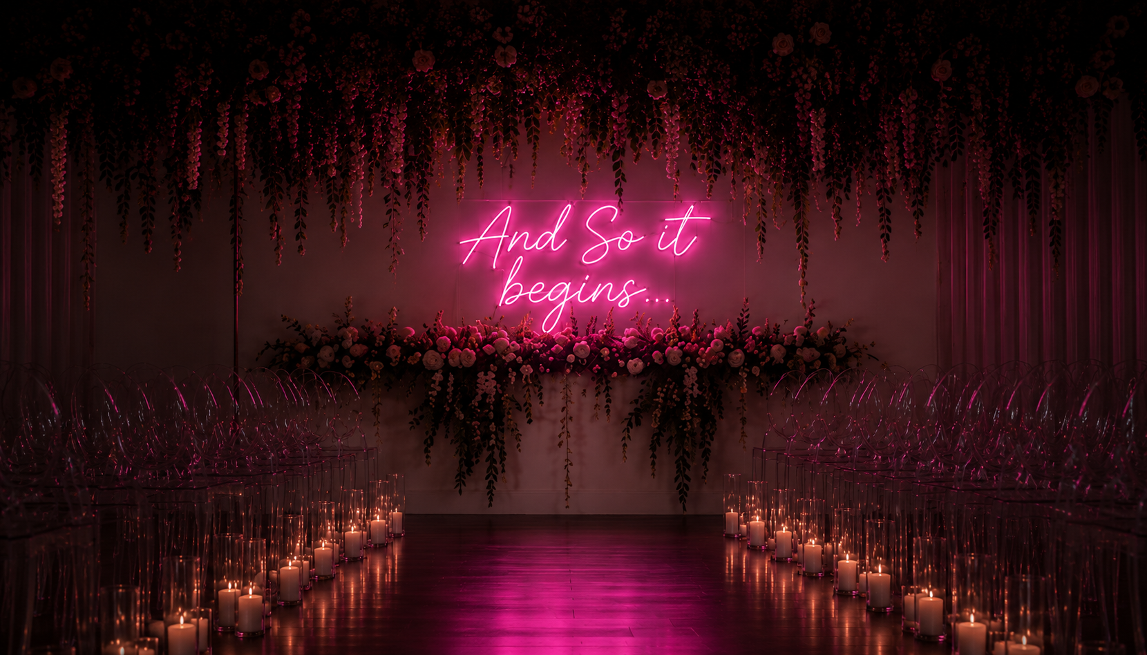 Warm white wedding neon sign reading And So It Begins within a flower-filled ceremony backdrop.